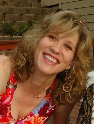 white woman with blond hair and sleeveless red floral dress.