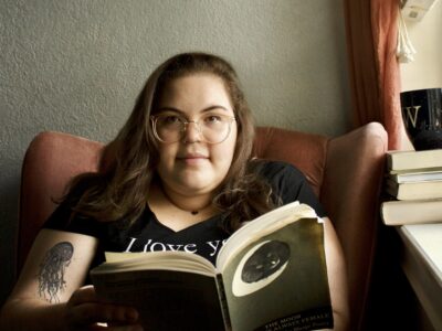 white woman with brown, long hair, glasses, in a black shirt holding a book.