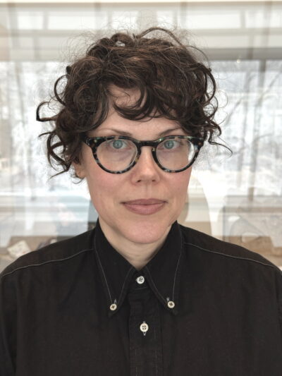female with dark brown short hair, black blouse, and black-rimmed glasses